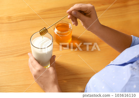 Woman adding honey to milk at table, closeup 103616110