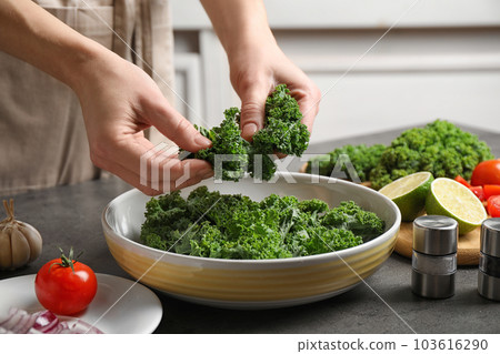 Woman cooking tasty kale salad on grey table, closeup 103616290
