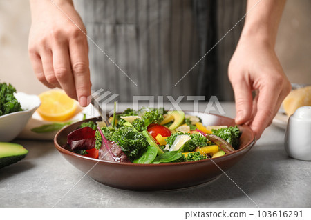 Woman cooking tasty kale salad on light grey table, closeup 103616291