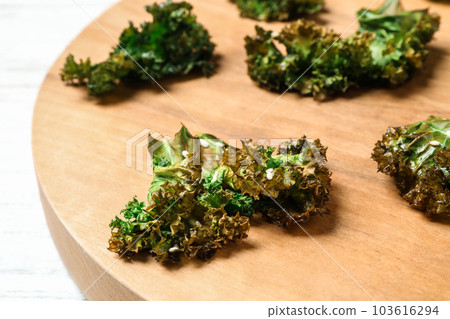 Tasty baked kale chips on wooden board, closeup Tasty baked kale chips on wooden board, closeup 103616294