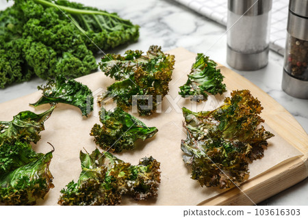 Tasty baked kale chips on wooden board 103616303