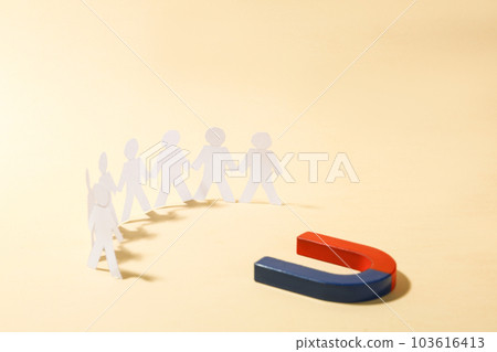 Magnet attracting paper people on beige background 103616413