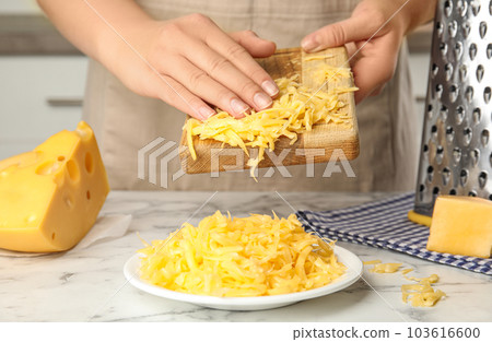 Woman with grated cheese at kitchen table, closeup 103616600