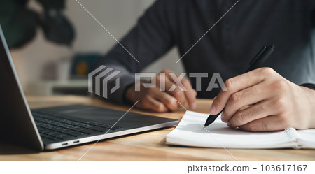 left handed man writes in a notebook on the table with laptop computer, Businessman. 103617167