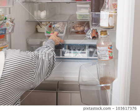 [A housewife takes out a tray from the refrigerator] 103617376