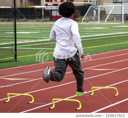 African American runners sprinting over small hurdles on a track 103617922