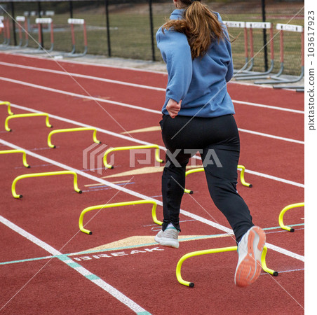 One female running over small hurdles on a track 103617923