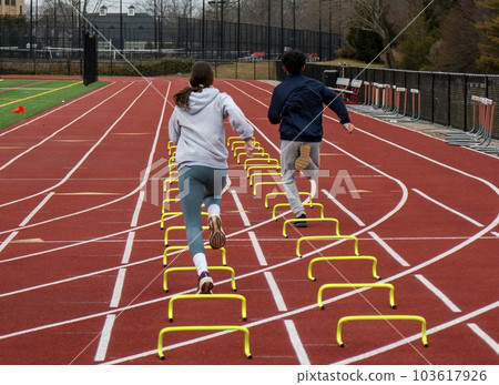 Two runners running over six inch mini hurdles on a track 103617926