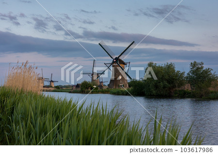 Beautiful wooden windmills at sunset in the Dutch village of Kinderdijk. Windmills run on the wind. The beautiful Dutch canals are filled with water. Beautiful sunset. 103617986