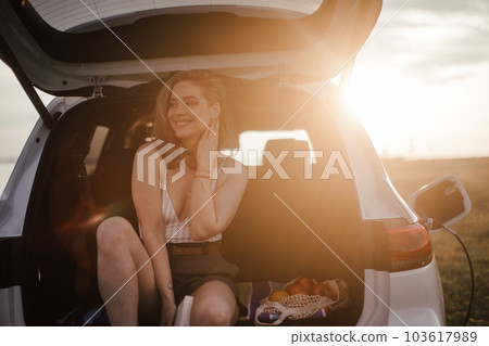 Young woman sitting in a car trunk, waiting for charging. 103617989