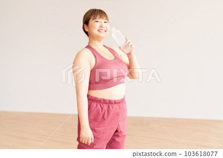 一個微笑的胖女孩拿著一瓶塑料水，一個大碼模特，在鍛煉 103618077