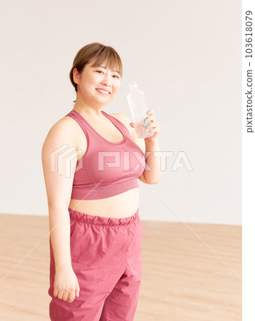 A smiling chubby woman holding a plastic bottle of water, a plus size model, exercising A smiling chubby woman holding a plastic bottle of water, a plus size model, exercising 103618079
