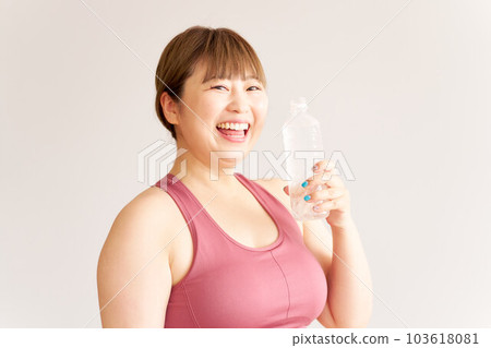 一個微笑的胖女孩拿著一瓶塑料水，一個大碼模特，在鍛煉 103618081