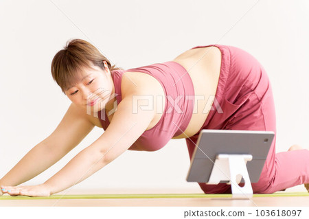 Plump young woman doing yoga while looking at a tablet Plus size model image 103618097