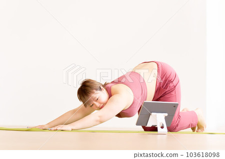 Plump young woman doing yoga while looking at a tablet Plus size model image 103618098