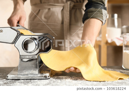 Woman preparing dough with pasta maker machine at table, closeup 103618224