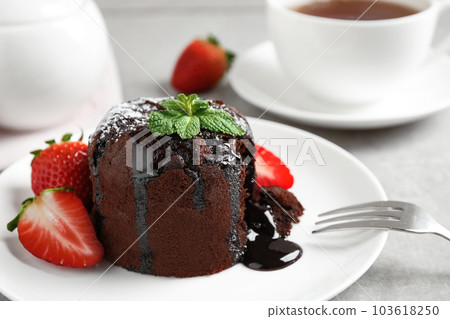 Delicious warm chocolate lava cake with mint and strawberries on table, closeup 103618250