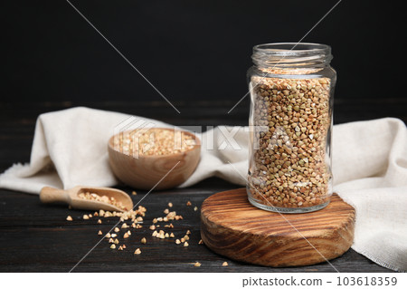 Jar with green buckwheat on black wooden table. Space for text 103618359