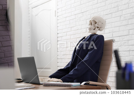 Human skeleton in suit using laptop at table in office Human skeleton in suit using laptop at table in office 103618445