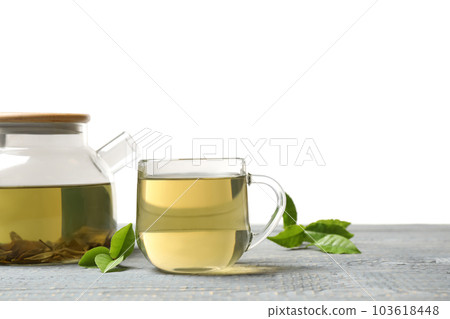 Cup of green tea, pot and leaves on grey wooden table 103618448