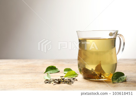 Cup of green tea, dry and fresh leaves on wooden table 103618451