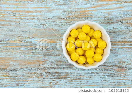 Delicious lemon chewing gums in bowl on light blue wooden background, top view. Space for text Delicious lemon chewing gums in bowl on light blue wooden background, top view. Space for text 103618553