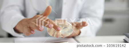 Female plastic surgeon touching silicone implant with finger 103619142