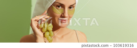 Woman using grapeseed-based eye patches on pastel green background. Natural sustainable skincare Woman using grapeseed-based eye patches on pastel green background. Natural sustainable skincare 103619316