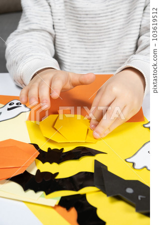 A child creates a pumpkin out of paper. Origami for Halloween, preparation A child creates a pumpkin out of paper. Origami for Halloween, preparation 103619512