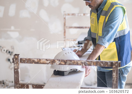 Experienced engineer correcting renovation plan stands near construction safety equipment skilled worker in vest getting ready for reconstruction of big house 103620572
