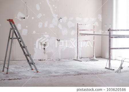 Ladder and construction equipment standing in empty room illuminated by bright sunlight shabby wall with holes and stains ready for painting renovation process in apartment Ladder and construction equipment standing in empty room illuminated by bright sunlight shabby wall with holes and stains ready for painting renovation process in apartment 103620586