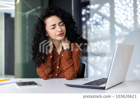 Overtired business woman working inside office with laptop, Hispanic female worker has severe neck pain, massaging muscles with hand 103620621