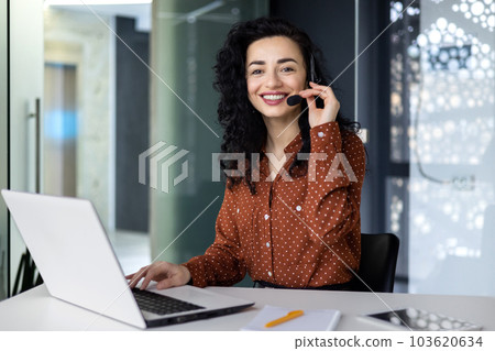 Portrait of Latin American business woman, office worker looking at camera and smiling, using headset and laptop for remote online communication, customer support tech call center worker 103620634