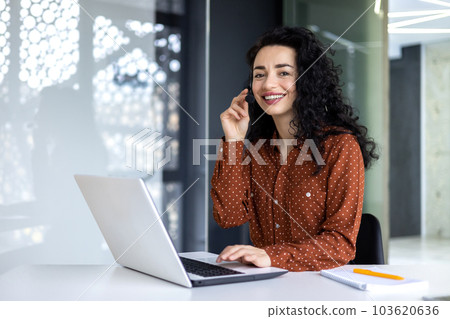 Portrait of Latin American business woman, office worker looking at camera and smiling, using headset and laptop for remote online communication, customer support tech call center worker 103620636