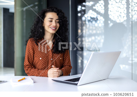 Happy and smiling hispanic businesswoman typing on laptop, office worker with curly hair happy with achievement results, at work inside office building. Happy and smiling hispanic businesswoman typing on laptop, office worker with curly hair happy with achievement results, at work inside office building. 103620651