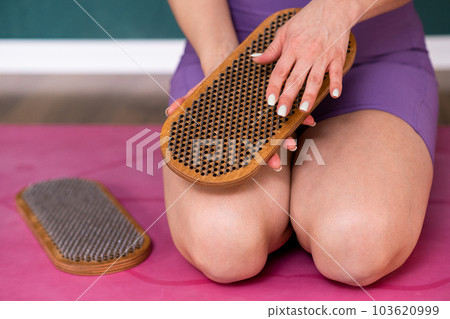 Woman touching sadhu nail board with hand sitting on pink mat in yoga studio female person in sportswear preparing for reflexotherapy practice to relax body closeup Woman touching sadhu nail board with hand sitting on pink mat in yoga studio female person in sportswear preparing for reflexotherapy practice to relax body closeup 103620999
