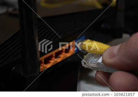 Close-up of a man's hand, fingers connecting a network cable to a router. 103621857