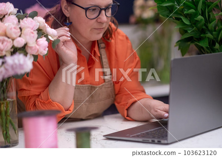 florist and business owner in the flower shop accepts orders using laptop and expertly creates arrangements, ready for pick-up or delivery. florist and business owner in the flower shop accepts orders using laptop and expertly creates arrangements, ready for pick-up or delivery. 103623120