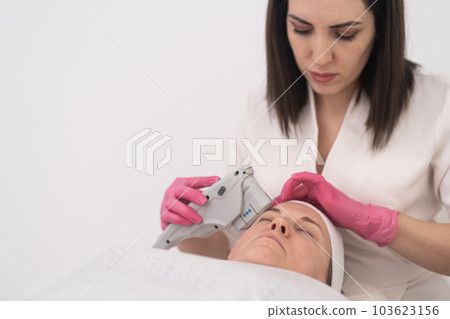 A SMAS face lifting laser procedure is administered to a relaxed female client with professional equipment and dermatologist at a beauty center.  103623156