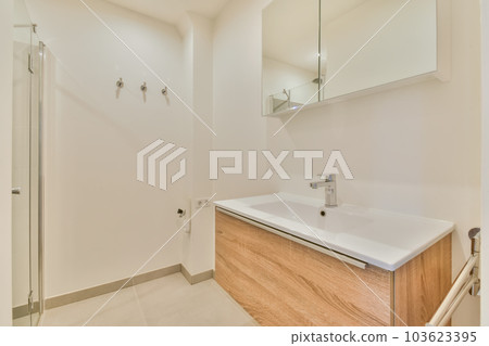 a bathroom with white walls and wood cabinetd vanity in the middle part of the room there is a mirror on the wall a bathroom with white walls and wood cabinetd vanity in the middle part of the room there is a mirror on the wall 103623395