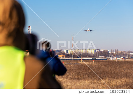 Group of many people watching planes landing and take off airport runway field planespotting conference warm morning time. Planespotters in safety vest waiting aicraft arrival approaching departure Group of many people watching planes landing and take off airport runway field planespotting conference warm morning time. Planespotters in safety vest waiting aicraft arrival approaching departure 103623534