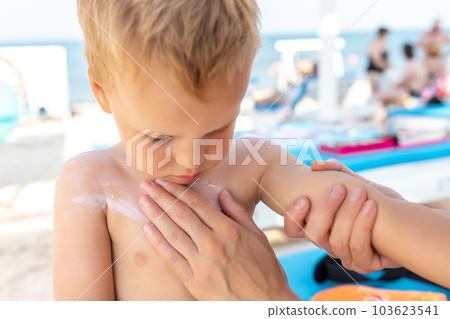 Mother applying sunscreen protection creme on cute little baby boy kid face. Mum using sunblocking lotion to protect baby from sun during summer sea vacation. Child healthcare travel vacation time Mother applying sunscreen protection creme on cute little baby boy kid face. Mum using sunblocking lotion to protect baby from sun during summer sea vacation. Child healthcare travel vacation time 103623541
