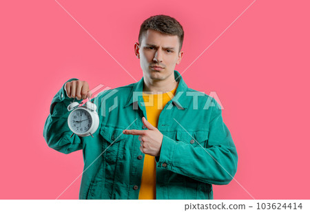 Woken up by alarm clock sleepy young man holding it in hand. Pink background 103624414