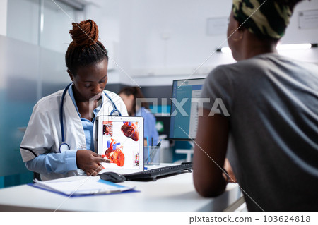 Doctor explaining heart informations to patient on tablet at clinic desk. Cardiologist providing healthcare cardiac diagnosis to african american woman at appointment checkup 103624818