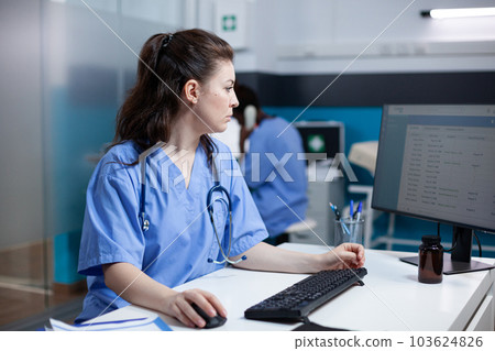 Caucasian nurse checking appointments list on computer monitor, sitting at clinic desk. Focused adult woman healthcare expert working in medical office with stethoscope around neck 103624826