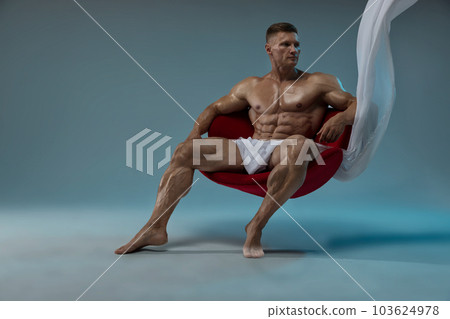A strong man of athletic build sits in a chair with a naked torso 103624978