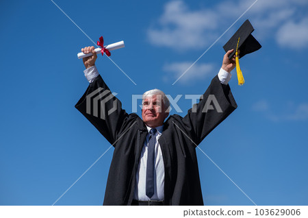 Elderly male graduate rejoices in receiving a diploma against a blue sky. Elderly male graduate rejoices in receiving a diploma against a blue sky. 103629006