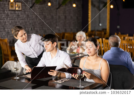 Young couple discussing menu with waitress at table in restaurant 103632017