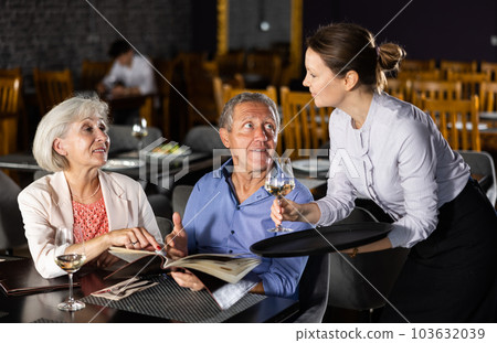 Mature man and woman reads menu and makes order to waitress Mature man and woman reads menu and makes order to waitress 103632039