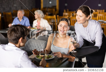 Waitress serving drinks to young couple sitting at table in restaurant Waitress serving drinks to young couple sitting at table in restaurant 103632138